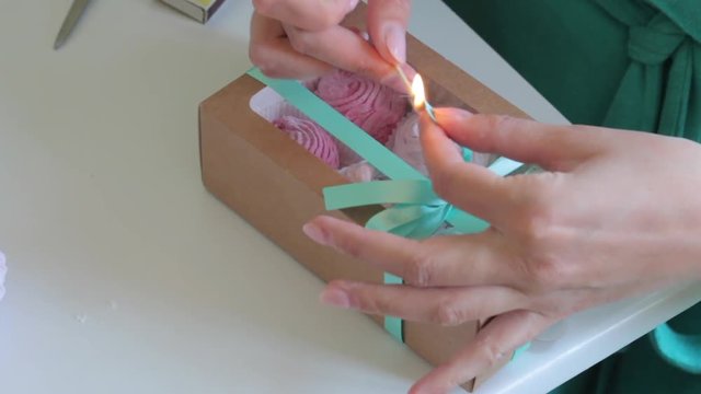 Homemade marshmallows of different colors in a gift box. A woman tied a box with a braid, tied a bow, and cauterized the ends of the ribbon with a match.