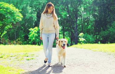 Woman owner walking with her Golden Retriever dog on leash in summer day