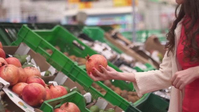 Close up, supermarket, market, grocery store slender attractive girl woman chooses colorful vegetables fruits pomegranates and puts in the basket, the concept of healthy food and lifestyle