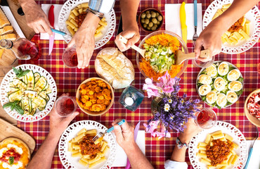 Aerial view of red table full of delicious food. Mediterranean diet. Pasta and vegetables. Group of people enjoying meal together