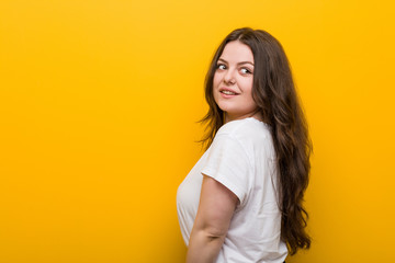 Young curvy plus size woman looks aside smiling, cheerful and pleasant.