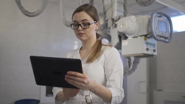 The young doctor checks the diagnosis on the tablet. X-ray machine.. 4k