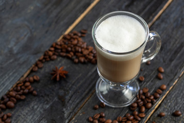 Coffee with milk in a glass on a wooden table with roasted coffee beans