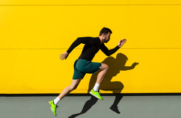 Portrait of male athlete running isolated on yellow wall.