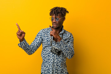 Young black rasta man wearing a vacation look shocked pointing with index fingers to a copy space.