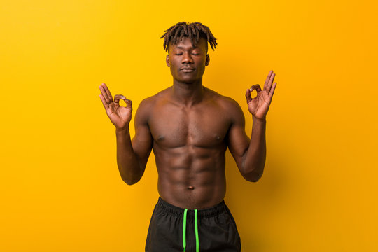 Young Black Man Shirtless Wearing Swimsuit Relaxes After Hard Working Day, He Is Performing Yoga.