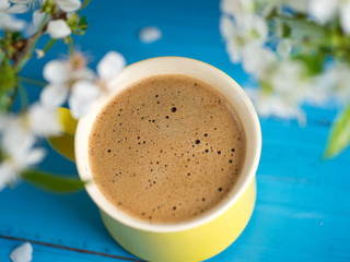 Spring coffee . Yellow Cup on blue background and cherry blossoms