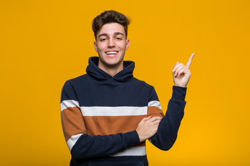 Young cool man wearing a hoodie smiling cheerfully pointing with forefinger away.