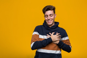 Young cool man wearing a hoodie laughing keeping hands on heart, concept of happiness.