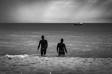 Two divers enter the sea where a fishing boat is waiting for the