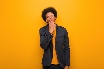 Young business african american man over an orange wall doubting and confused