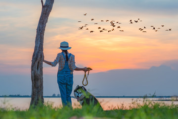 Naklejka na ściany i meble woman girl enjoy standing with a puppy dog at lake river with sunset sweet time, friendship and relationship together in comfortable time