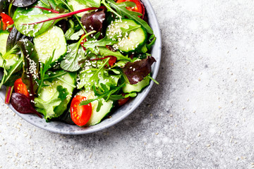 Vegetable salad in a glass bowl with greens, olive oil and sesame  on a gray background.Vegetarian. Concept for a tasty and healthy meal. Copy space for Text.Top view.