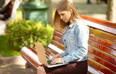 Young businesswoman sitting in the park and working with laptop. Business, education, lifestyle concept.