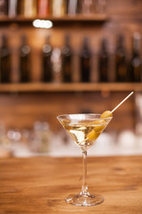 Glass of dry martini with green olives on a rustic wooden bar counter