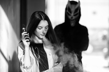 Vape teenager and death. Young cute girl in a dress an electronic cigarette near the wall in front...