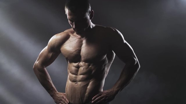 Handsome shirtless athletic man posing on a dark background. Athletic bodybuilder posing