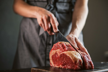 cook cuts raw meat for steaks