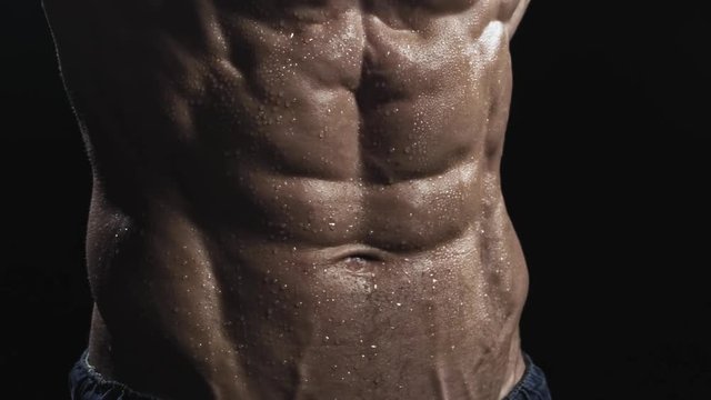 Close-up of abs of unrecognizable shirtless muscular man.  Muscle man posing on a black background, shows his muscles. The concept of bodybuilding