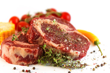 set for cooking a festive dinner for two. two raw marbled beef steaks, spices, vegetables and a grill pan with a meat fork. all on a white background