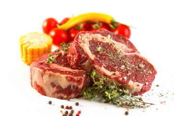 set for cooking a festive dinner for two. two raw marbled beef steaks, spices, vegetables and a grill pan with a meat fork. all on a white background
