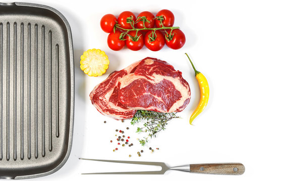 Set For Cooking A Festive Dinner For Two. Two Raw Marbled Beef Steaks, Spices, Vegetables And A Grill Pan With A Meat Fork. All On A White Background