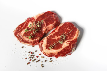 two fresh marbled beef steaks on a white plate with a sprig of rosemary, salt and different varieties of peppers