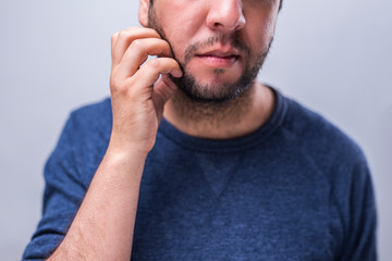 Closeup to young man scratching beard, thoughtful gesture, indoors studio shot