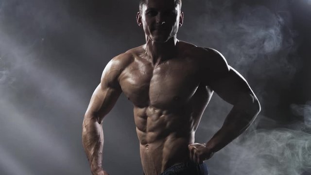 Bodybuilder posing in studio on a dark background. Handsome shirtless athletic man