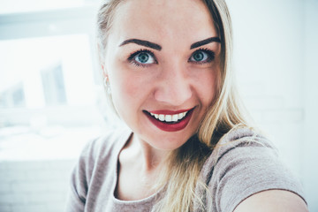 Smiling young european blonde woman making selfie in her studio apartment