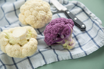 Bunter Blumenkohl in Lila und Weiß auf Geschirrtuch mit Messer auf Pastell Grün Hintergrund