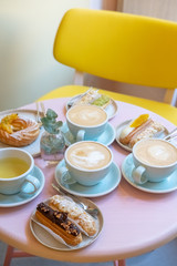 Cafe table with cups of coffee, eclairs and cake