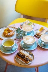 Cafe table with cups of coffee, eclairs and cake
