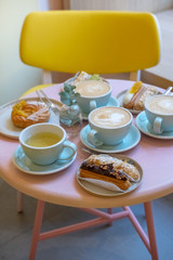Cafe table with cups of coffee, eclairs and cake