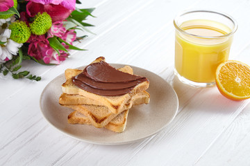 Close up view on toast with nut butter. Breakfast concept with orang juice, flowers and toast on white wooden background. Traditional summer breakfast. Composition with copy space for design