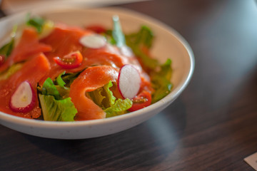 Fresh smoke salmon salad with spinach , lettuce, tomatoes ,red onions , with olive oil in a white plate . Home made food for a tasty and healthy meal Concept .