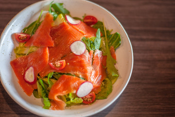 Fresh smoke salmon salad with spinach , lettuce, tomatoes ,red onions , with olive oil in a white plate . Home made food for a tasty and healthy meal Concept .