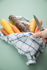 Frau kocht bunte Urkarotte und Möhren in Lila, Orange und Gelb auf Geschirrtuch mit Messer auf...