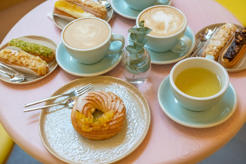 Cafe table with cups of coffee, eclairs and cake