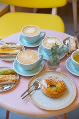 Cafe table with cups of coffee, eclairs and cake