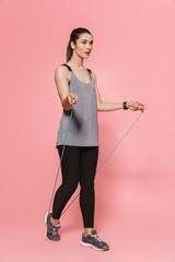 Young pretty fitness woman make sport exercises with skipping jumping rope isolated over pink wall...