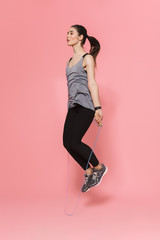 Young pretty fitness woman make sport exercises with skipping jumping rope isolated over pink wall background.
