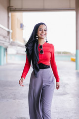 Fototapeta premium Fashion portrait of a ravishing Muslim Arab Middle Eastern female in an elegant trendy Muslim outfit and a hijab headscarf walking down a car park during the day. She is tall and stylish.