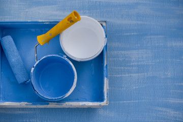 blue and white paint in cans top view. roller with a yellow handle for painting walls