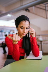Obraz premium An enthusiastic representative business visionary who is a Muslim lady in a hijab headscarf is talking to her client over the phone. She looks stunning in her red dress.