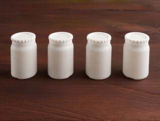 Four small plastic white banks with lids on a brown wooden background
