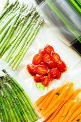 Vacuum sealed vegetables , carrots, asparagus, tomatoes,  on a gray background top view, ready to...