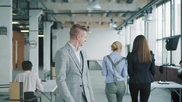 a young businessman in a jacket goes to the office to meet two employees, flirts, turns around after them as they pass by him. Creative coworking in a loft style. Office space