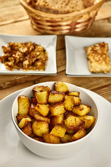 Roasted potatoes in a white bowl with rosemary and dill at next to fried onions and fish in batter on wooden background. Close-up rustic composition.