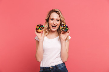 Portrait of gorgeous blond woman 20s wearing casual t-shirt smiling while holding tasty sweet donuts